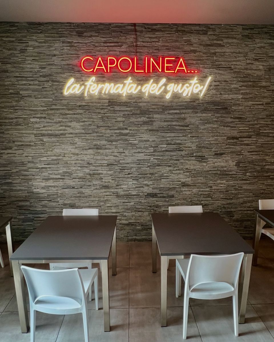 La sala della Pizzeria Capolinea: parete in pietra, tavoli e l'insegna al neon «Capolinea… la fermata del gusto!»