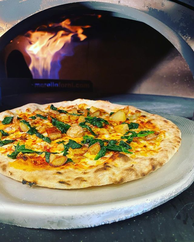 Una pizza sulla pala, appena sfornata, con le fiamme del forno dietro